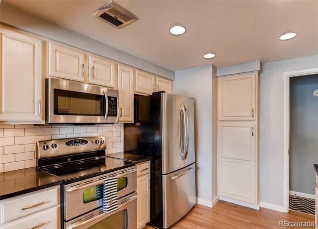 Kitchen with cream cabinets, stainless steel appliances, subway tile backsplash, and wood flooring.