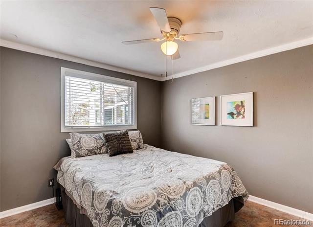 Bedroom with a patterned bedspread, window blinds, framed art, and a ceiling fan.