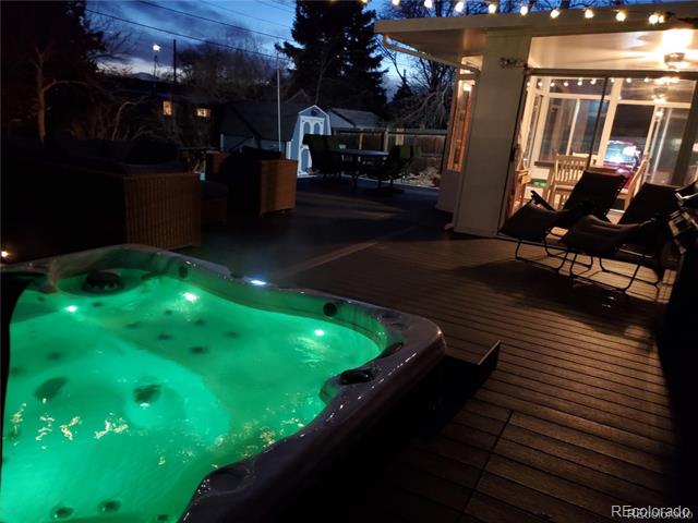 Glowing green hot tub on a wooden deck beside a warmly lit patio.