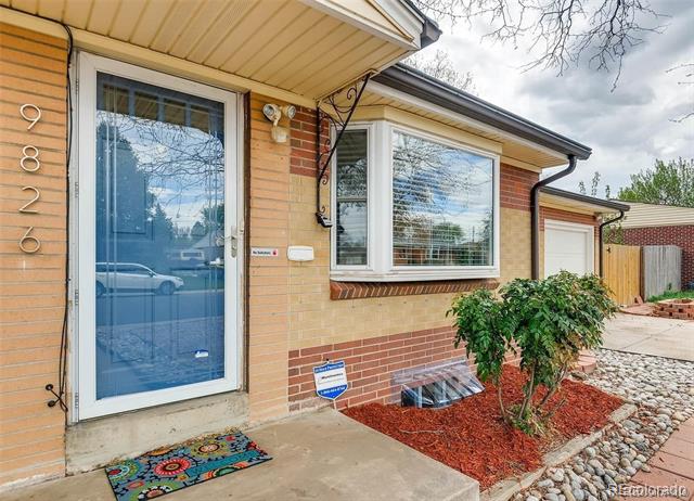 Front entrance with blue glass storm door, brick siding, large window, and landscaped shrub bed.