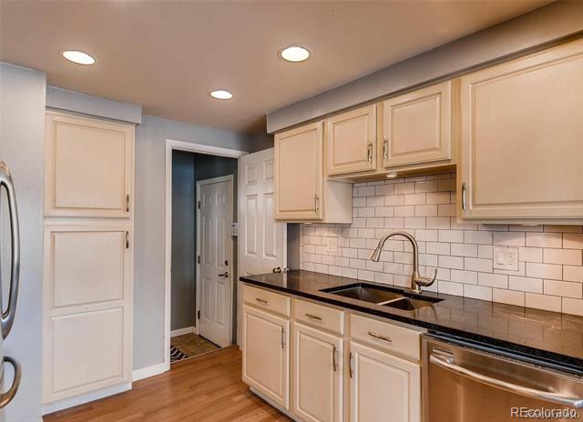 Kitchen with white cabinetry, dark counters, subway-tile backsplash, and stainless steel dishwasher.