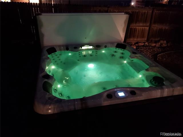 Outdoor hot tub glowing green at night, with multiple seats and jets in a fenced yard.