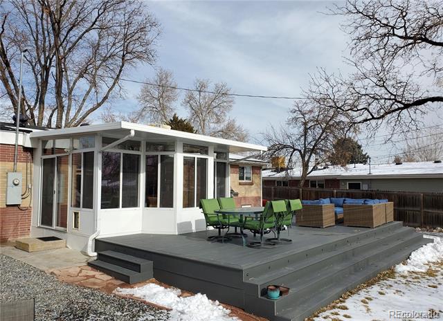 Home’s raised gray deck with green dining furniture, a sunroom, and a hot tub.