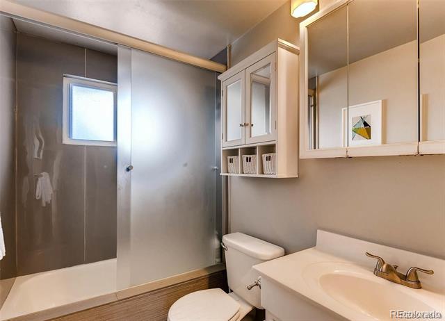 Bathroom with a glass shower, small window, white toilet, and wide vanity with wall mirror.