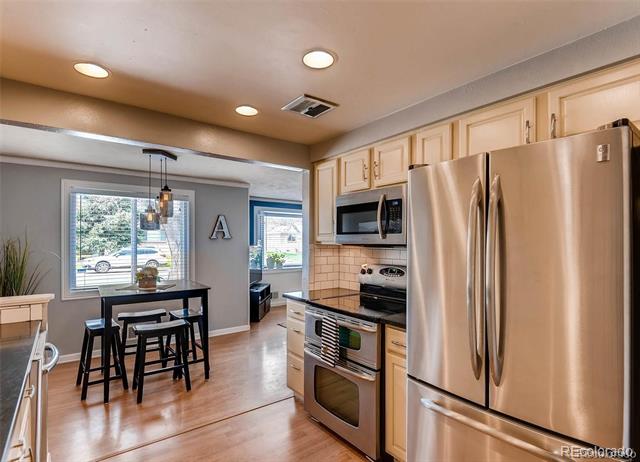 Kitchen with stainless steel appliances and light wood cabinets, adjoining a dining area with a small table.