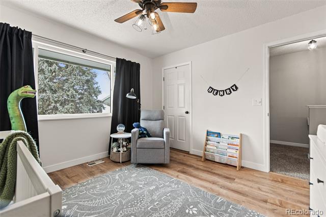 Child’s bedroom with a white crib, gray armchair, window, and wood-look flooring.