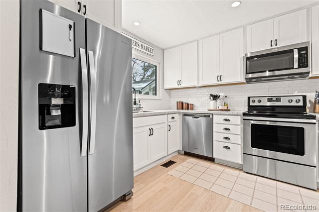 Kitchen with white cabinets, stainless steel appliances, and pale wood flooring.