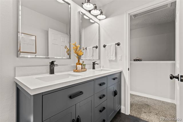 Bathroom with a gray double vanity, white countertop, large mirrors, and a bathtub through the doorway.