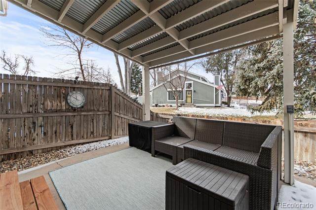 Covered patio with dark wicker seating and a view of a neighboring home beyond the fence.