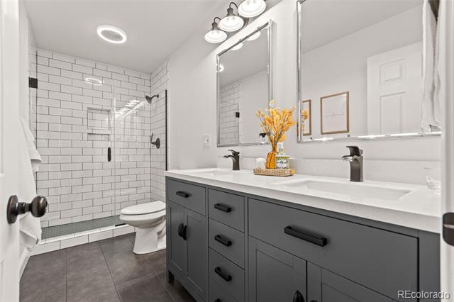 Bathroom with a gray double vanity, large mirrors, and a white subway-tile shower.