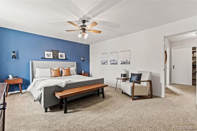 Staged bedroom with a blue accent wall, gray bed, wooden bench, and white armchair.