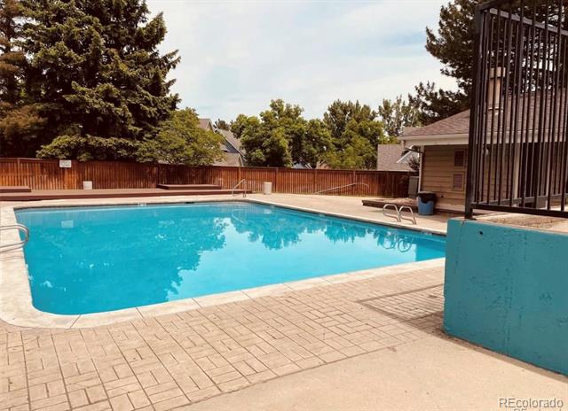 Outdoor swimming pool with a paved deck, wooden fencing, and mature trees.