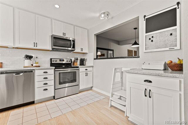 White kitchen with stainless steel appliances, tiled backsplash, and a small step stool beside the counter.