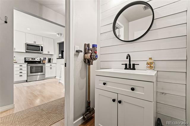 Bathroom vanity with black faucet and round mirror, opening to a white kitchen.