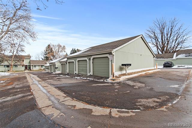 Row of sage-green garages with individual doors beside a paved parking area.