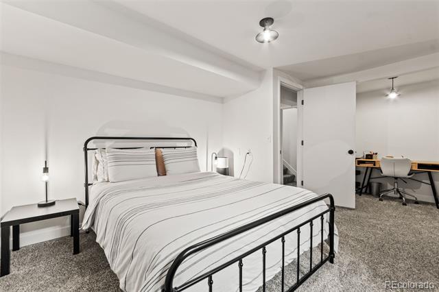 Bedroom with a black metal bed, striped white bedding, and an adjoining desk area.