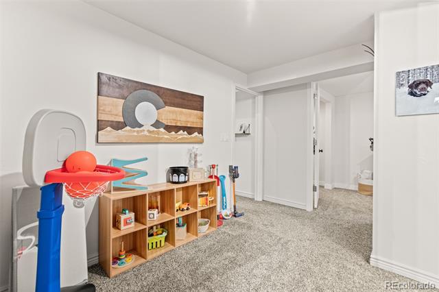 Carpeted playroom with a child-sized basketball hoop and wooden toy shelves beneath landscape artwork.
