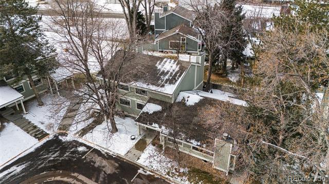 Aerial view of a green home and adjoining buildings with snow-dusted roofs among leafless trees.