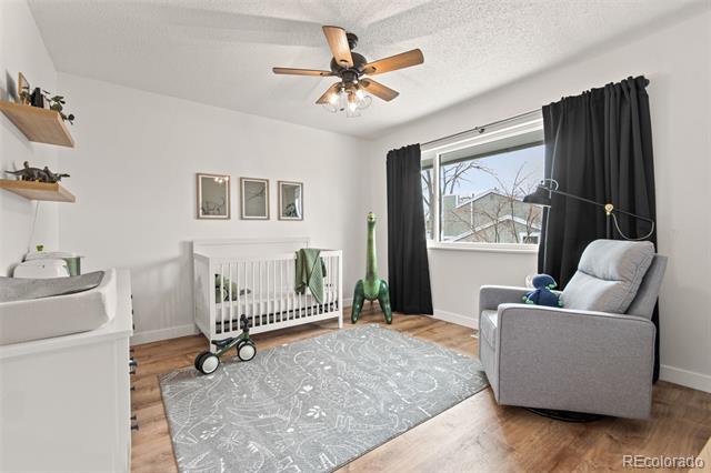 Nursery with a white crib, gray glider, black curtains, and a patterned rug.