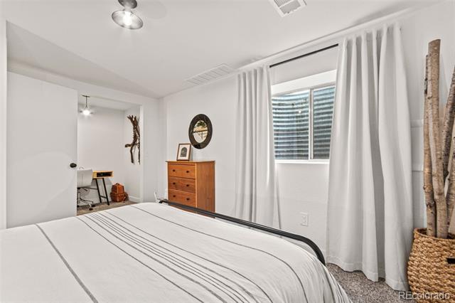 Bedroom with a white bed, wooden dresser, round mirror, and curtained window.