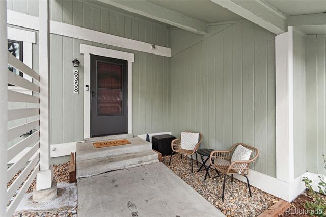 Covered front porch with a dark door, concrete steps, and two wicker chairs.