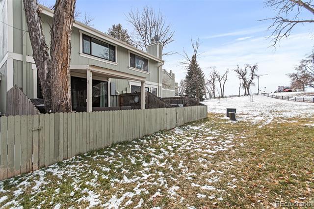 Attached home beside a fenced yard with patchy snow and leafless trees.