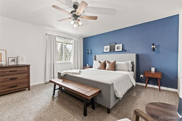 Bedroom with a gray upholstered bed, blue accent wall, wooden bench, and ceiling fan.