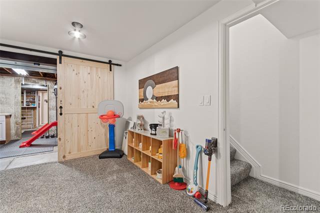 Basement playroom with a wood barn door, toy storage cubbies, and stairs.