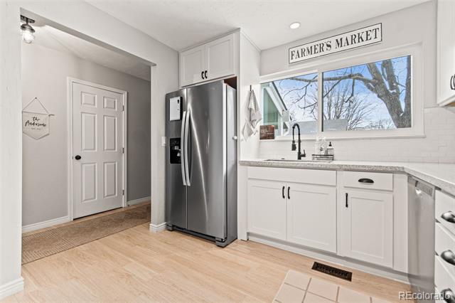 White kitchen with stainless steel refrigerator, light wood floors, and a sink beneath a large window.