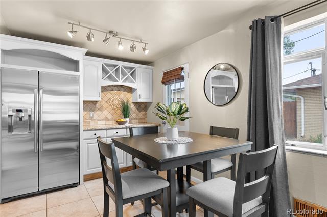 Dining area with a dark table and four chairs beside a white kitchen and stainless steel refrigerator.