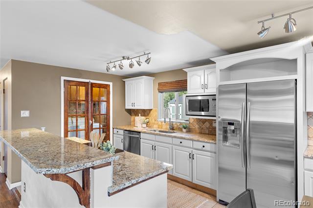 Kitchen with granite island, white cabinets, stainless steel appliances, and a glass-paned wooden door.