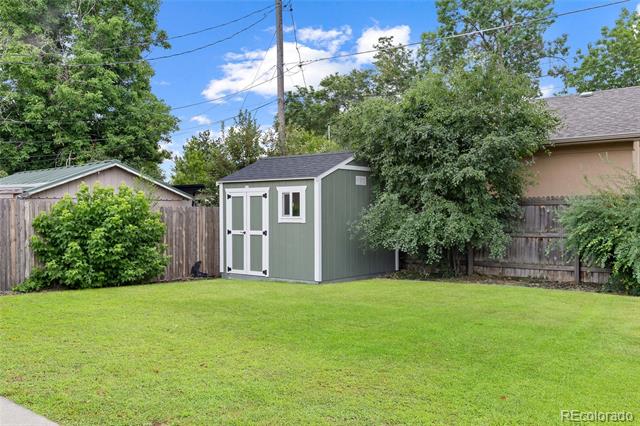 Fenced backyard with a green storage shed, broad lawn, and mature trees.