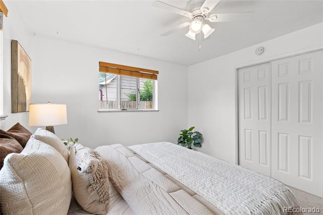 Furnished bedroom with a white bed, ceiling fan, window with wooden blind, and sliding closet doors.