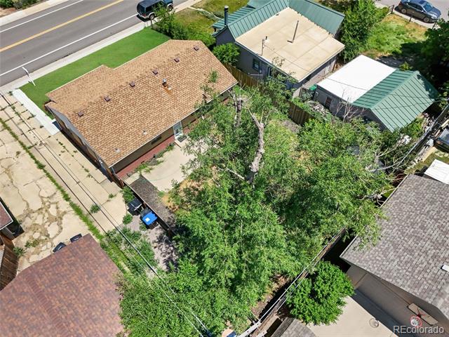 Aerial view of a brown-roofed house and tree-filled yard beside a street.