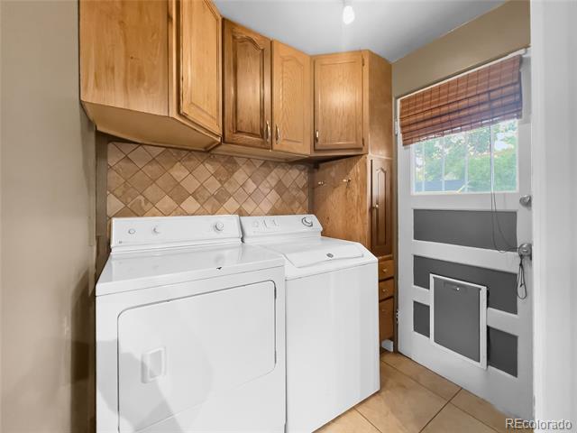 Laundry room with white washer and dryer, wood cabinets, and a glass door with a pet door.