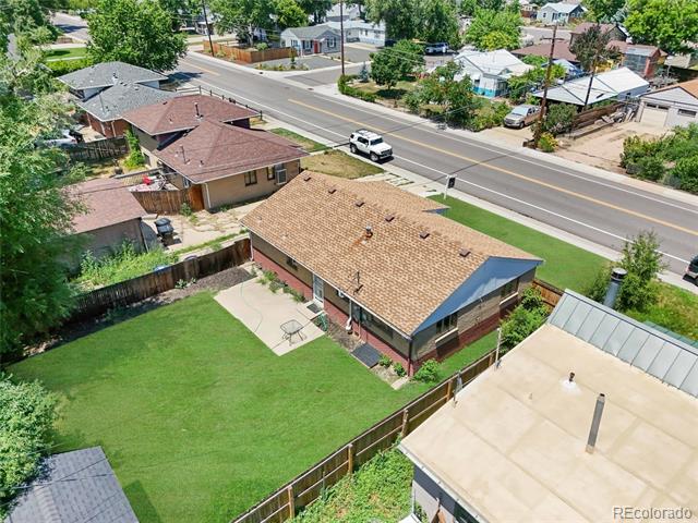 Aerial view of a brick home with a tan roof, fenced lawn, and patio beside a residential street.