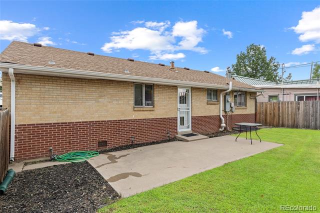 Brick house rear exterior with a concrete patio, white entry door, and green lawn.