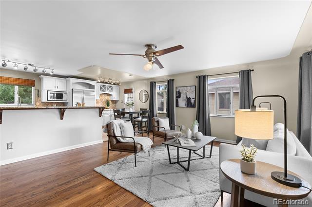 Living room with hardwood floors, a gray rug, white sofa, and open kitchen with white cabinetry.