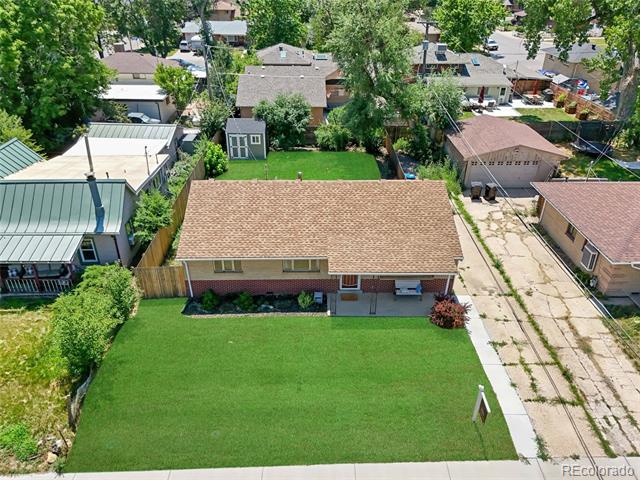 Aerial view of a single-story home with a broad front lawn, fenced backyard, and detached shed.