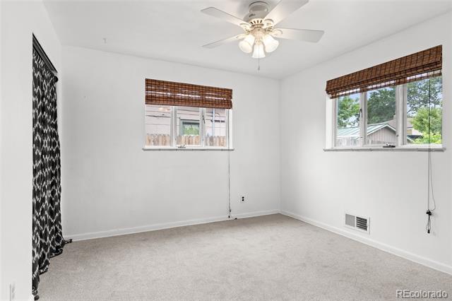 Empty carpeted bedroom with two windows, woven shades, and a ceiling fan with light.