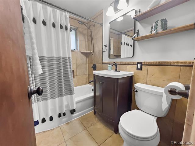 Bathroom with tan tile, striped shower curtain, dark wood vanity, and white toilet.