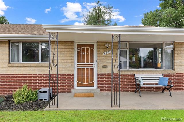 Single-story brick house with a white entry door, decorative porch supports, and a bench.