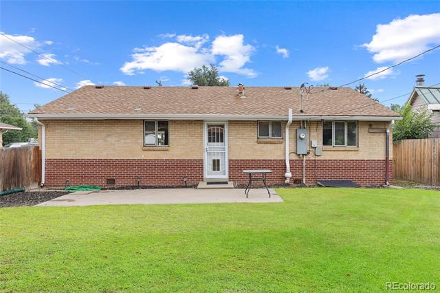 Rear exterior of a brick house with a broad lawn and small patio.