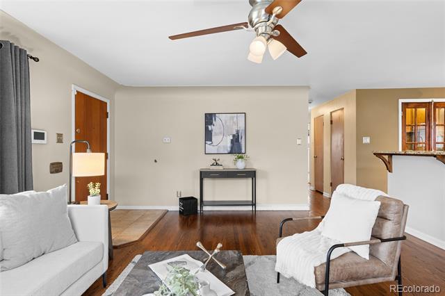 Living room with dark hardwood floors, gray seating, a patterned rug, and a ceiling fan.