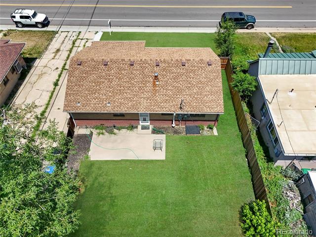 Aerial view of a brick house and spacious backyard with a concrete patio beside the road.