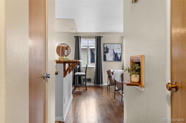 Furnished living area with wood floors, dark-curtained window, and a chair, viewed through an open doorway.