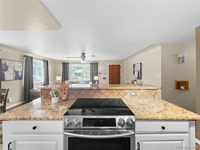 Open kitchen with granite island and stainless steel range overlooking a furnished living area.