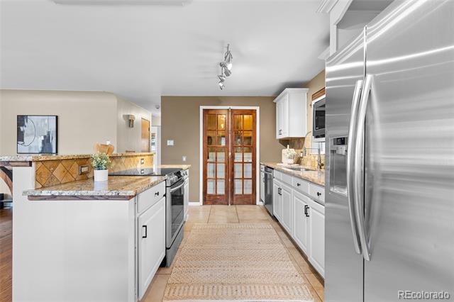 Kitchen with white cabinetry, granite island, stainless steel refrigerator, and glass-paneled double doors.