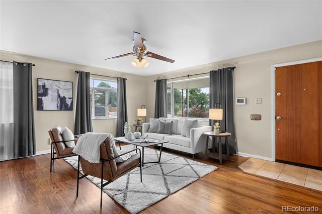 Living room with gray sofa, leather chairs, hardwood floors, and large curtained windows.