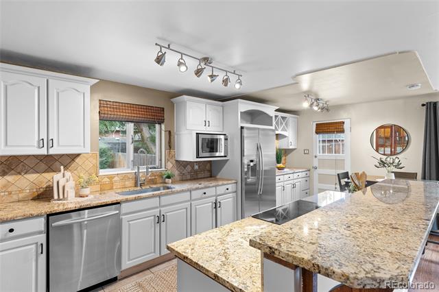 Kitchen with white cabinets, stainless steel appliances, and a large granite island with a cooktop.